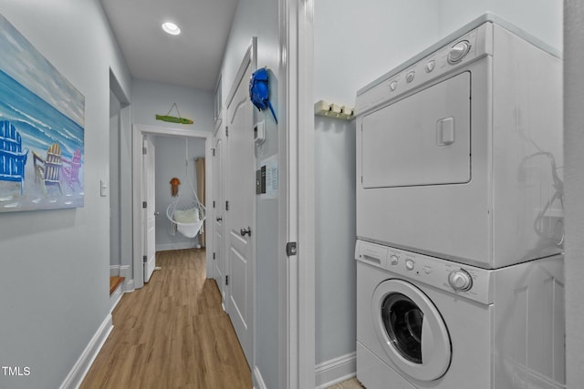 laundry area with baseboards, recessed lighting, stacked washing maching and dryer, light wood-style floors, and laundry area