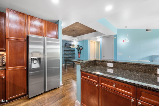 kitchen featuring stainless steel refrigerator with ice dispenser, dark stone countertops, wood finished floors, and visible vents
