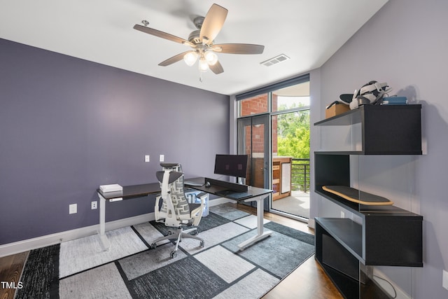 office space featuring a wall of windows, a ceiling fan, baseboards, wood finished floors, and visible vents