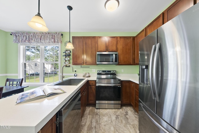 kitchen featuring appliances with stainless steel finishes, a sink, light countertops, decorative light fixtures, and brown cabinetry
