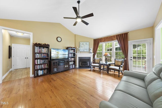 living area with ceiling fan, a fireplace, light wood finished floors, vaulted ceiling, and baseboards