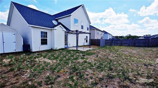 back of house with roof with shingles, a storage shed, a patio area, fence, and a pergola
