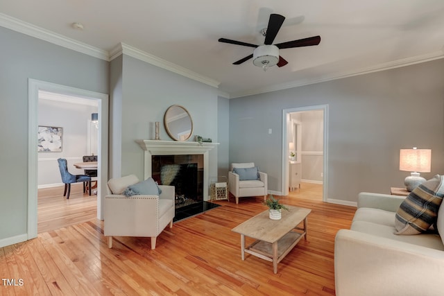 living area with crown molding, light wood-type flooring, a tile fireplace, a ceiling fan, and baseboards