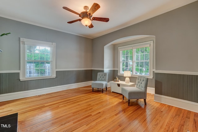 living area featuring hardwood / wood-style floors, wainscoting, ornamental molding, ceiling fan, and arched walkways