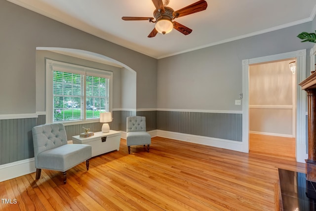 living area with wood-type flooring, wainscoting, ceiling fan, ornamental molding, and arched walkways