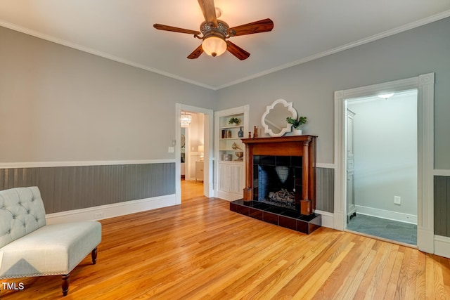 sitting room featuring wood finished floors, a ceiling fan, ornamental molding, a tiled fireplace, and built in shelves