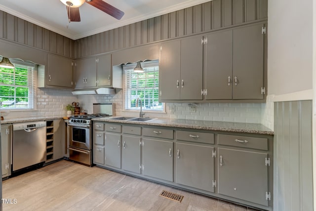 kitchen featuring appliances with stainless steel finishes, gray cabinetry, crown molding, decorative backsplash, and a sink