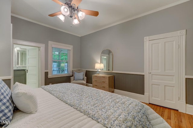 bedroom with wood finished floors, wainscoting, ornamental molding, and a ceiling fan