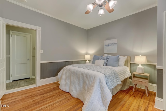 bedroom featuring wood-type flooring, wainscoting, crown molding, and ceiling fan