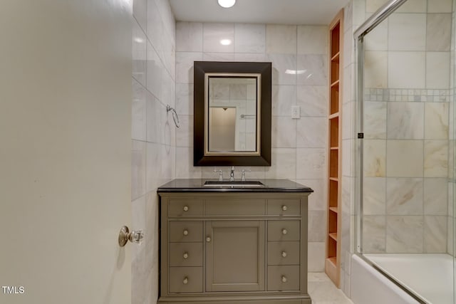 full bath featuring tile walls, vanity, and shower / bath combination with glass door