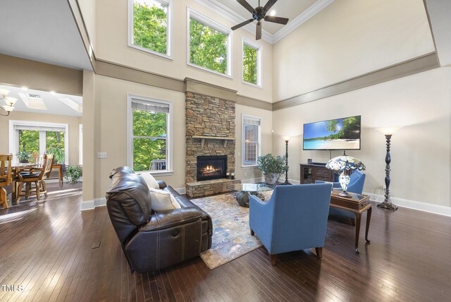 living room with a ceiling fan, a towering ceiling, a fireplace, baseboards, and wood-type flooring
