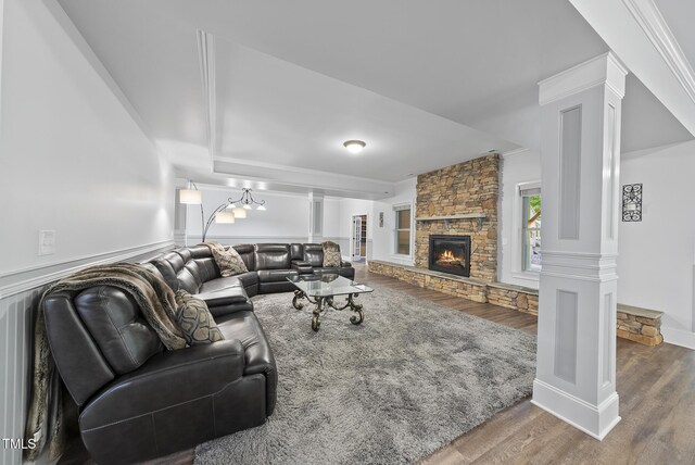 living room featuring ornamental molding, a stone fireplace, ornate columns, and wood finished floors