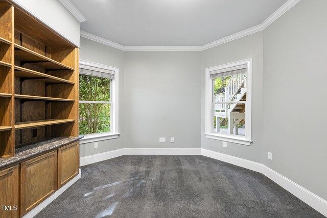 spare room featuring baseboards, ornamental molding, dark carpet, and a wealth of natural light