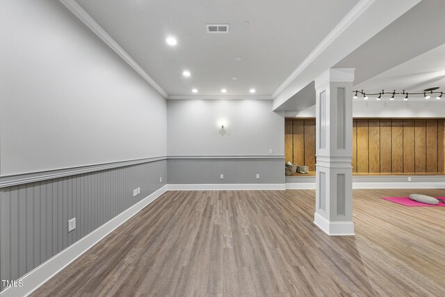 basement featuring a wainscoted wall, baseboards, wood finished floors, visible vents, and ornamental molding