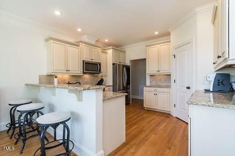 kitchen with tasteful backsplash, ornamental molding, light wood-type flooring, a peninsula, and stainless steel appliances