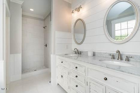 full bath featuring tile patterned floors, double vanity, a tile shower, and a sink