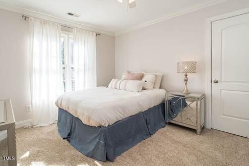 bedroom featuring light carpet, ceiling fan, ornamental molding, and visible vents