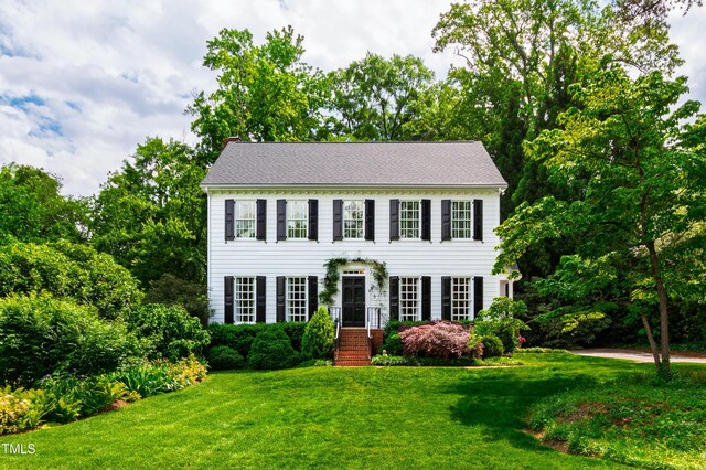 colonial home featuring a chimney and a front lawn