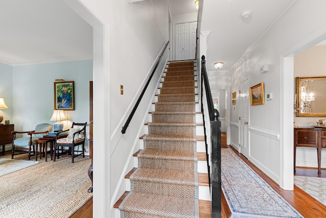 stairway featuring wood finished floors, crown molding, and a decorative wall