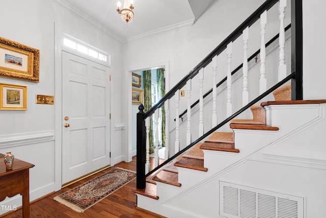 foyer with stairs, wood finished floors, crown molding, and a chandelier
