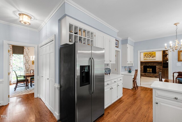 kitchen with stainless steel fridge with ice dispenser, a chandelier, a brick fireplace, white cabinets, and crown molding