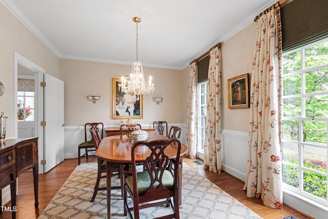 dining room with ornamental molding, wood finished floors, a chandelier, and a wainscoted wall