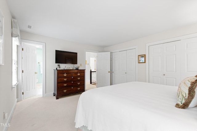 bedroom with two closets, light colored carpet, and baseboards