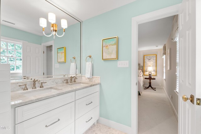 ensuite bathroom with double vanity, a chandelier, and baseboards