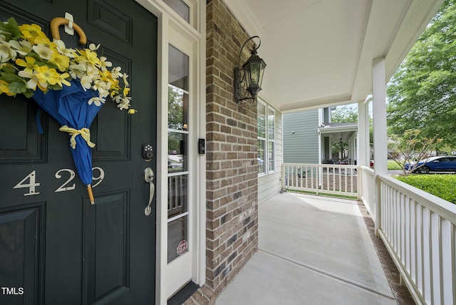 view of exterior entry featuring brick siding and a porch