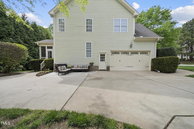 rear view of property with a garage, outdoor lounge area, driveway, and a shingled roof