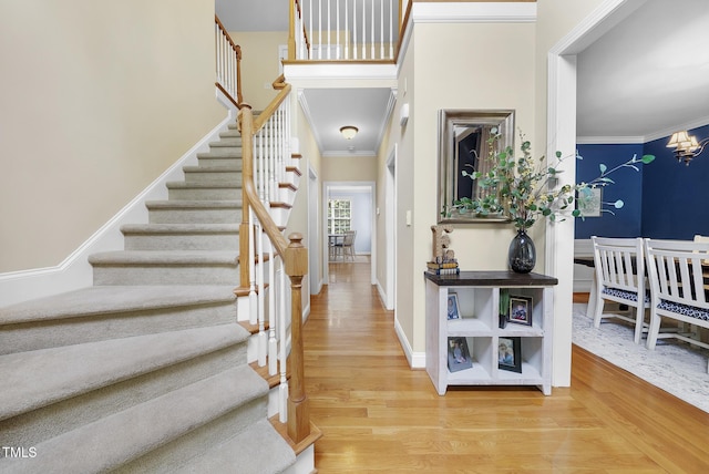 foyer entrance featuring stairway, crown molding, wood finished floors, and an inviting chandelier