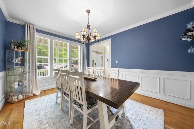 dining space featuring a wainscoted wall, a notable chandelier, wood finished floors, a decorative wall, and ornamental molding