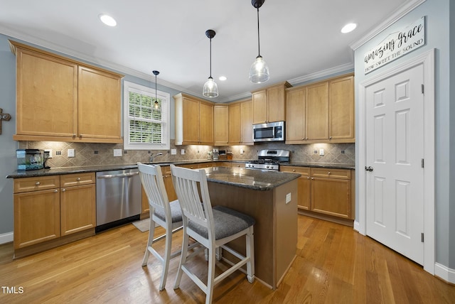 kitchen with a sink, light wood-style flooring, backsplash, appliances with stainless steel finishes, and a kitchen island