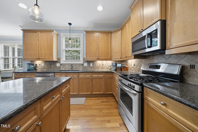 kitchen featuring light wood finished floors, a sink, decorative backsplash, hanging light fixtures, and appliances with stainless steel finishes