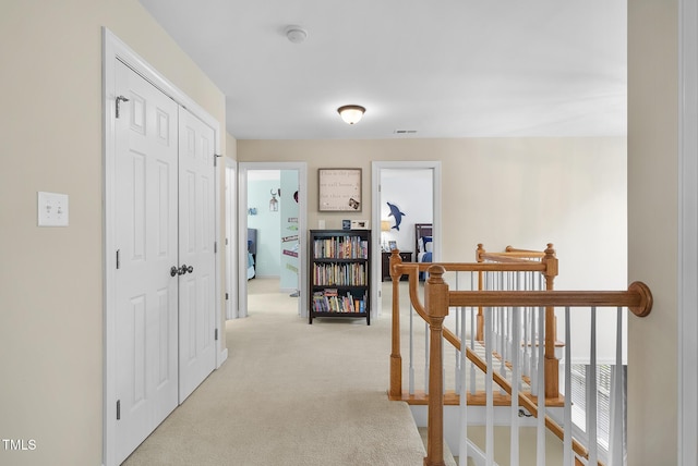 hallway with light carpet, visible vents, and an upstairs landing