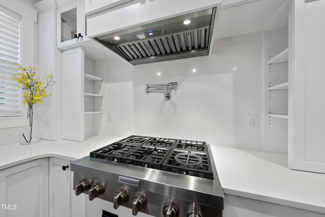6024 Lunenburg Dr, Raleigh, NC 27603 - kitchen featuring wall chimney exhaust hood, white cabinets, stainless steel gas stovetop, glass insert cabinets, and light countertops
