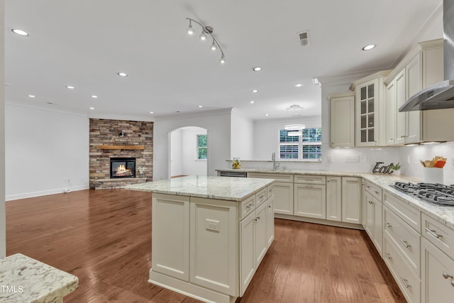 644 Angelica Cir, Cary, NC 27518 - kitchen with wall chimney range hood, stainless steel gas cooktop, a kitchen island, a sink, and open floor plan