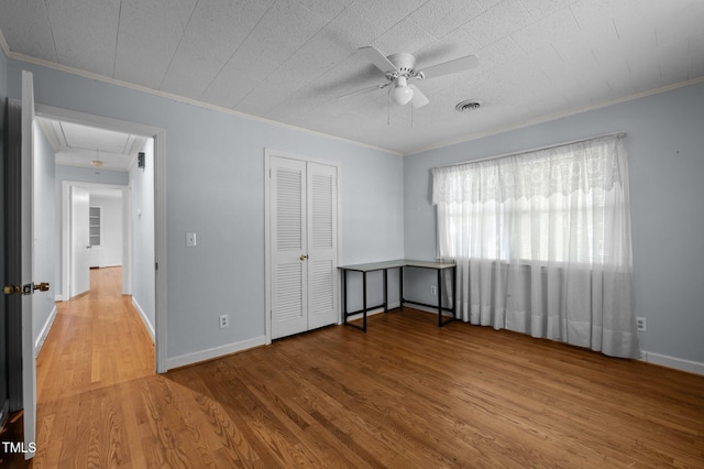 unfurnished bedroom featuring attic access, crown molding, wood finished floors, and visible vents
