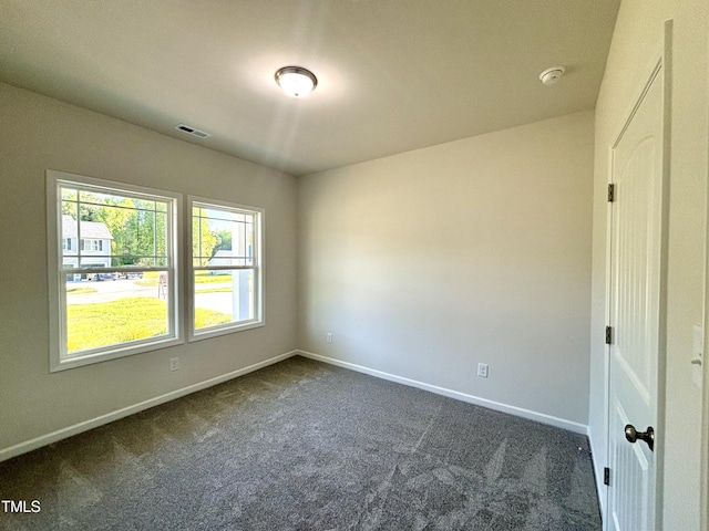 empty room with dark colored carpet, visible vents, and baseboards
