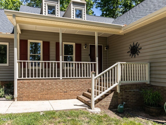 entrance to property with a porch and a shingled roof