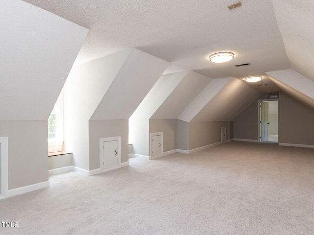 additional living space featuring carpet flooring, a textured ceiling, vaulted ceiling, and visible vents
