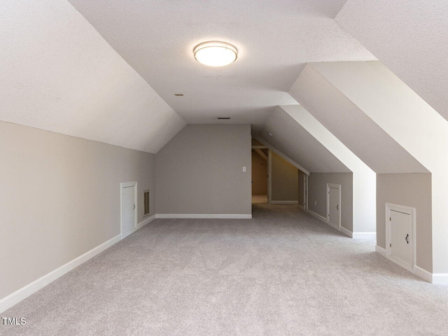 bonus room featuring baseboards, lofted ceiling, a textured ceiling, and light colored carpet