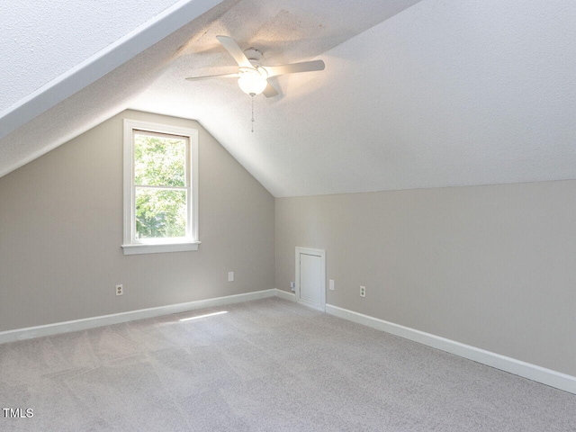 additional living space with light carpet, a textured ceiling, a ceiling fan, baseboards, and lofted ceiling