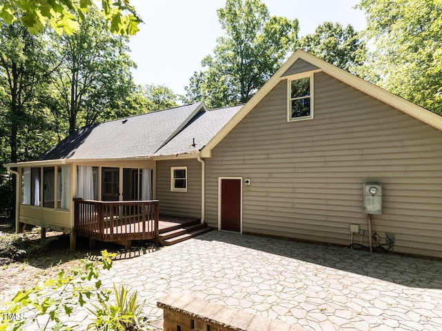 rear view of property with roof with shingles, a wooden deck, a sunroom, and a patio area