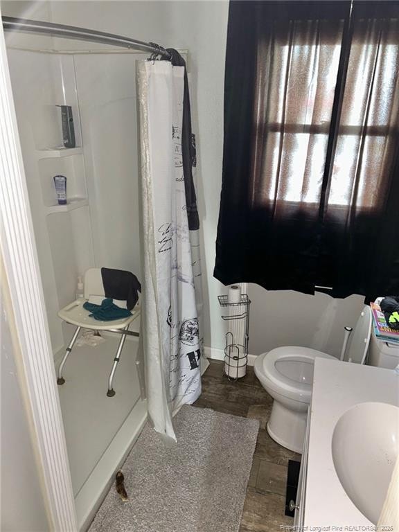full bathroom with toilet, wood finished floors, a shower with shower curtain, a sink, and baseboards