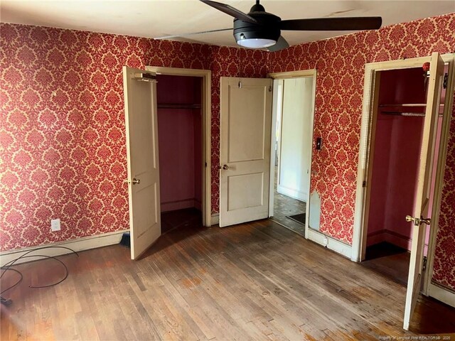 unfurnished bedroom featuring wallpapered walls, baseboards, hardwood / wood-style floors, and a ceiling fan