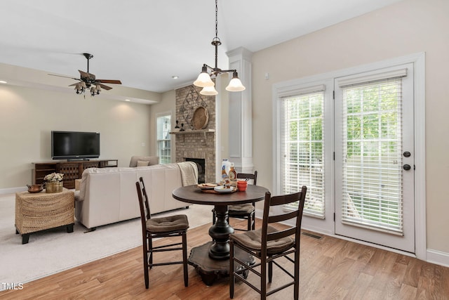 dining room featuring light wood-style flooring, a large fireplace, ceiling fan, and visible vents