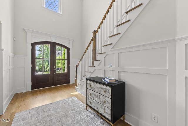 entrance foyer featuring a decorative wall, healthy amount of natural light, french doors, wood finished floors, and a high ceiling