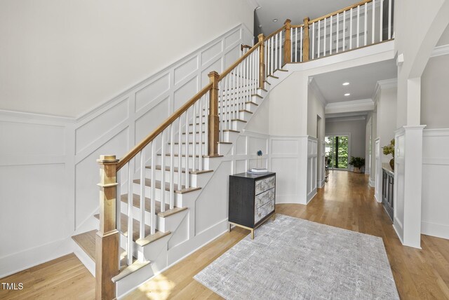 stairs with a decorative wall, wood finished floors, crown molding, and a towering ceiling