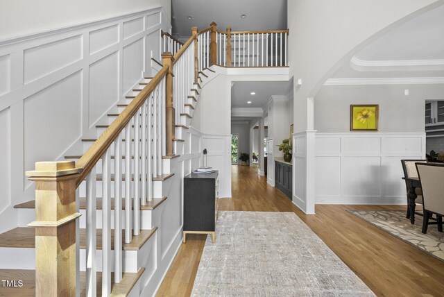 entrance foyer with ornamental molding, light wood-type flooring, arched walkways, a towering ceiling, and stairs